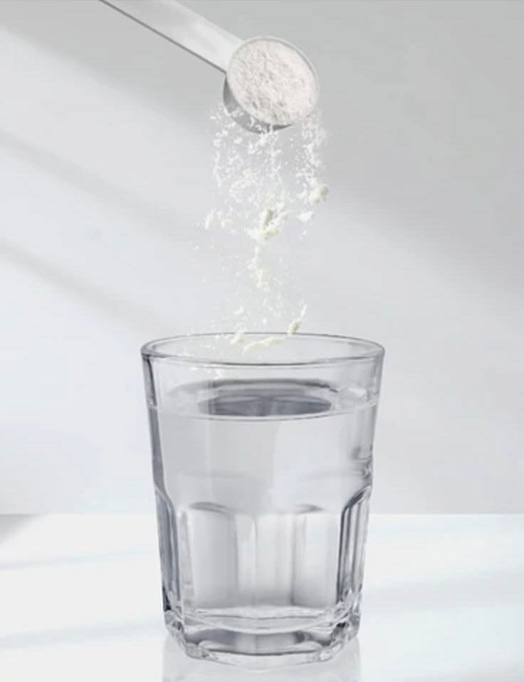 Cacito de creatina monohidrato cayendo en un vaso de agua