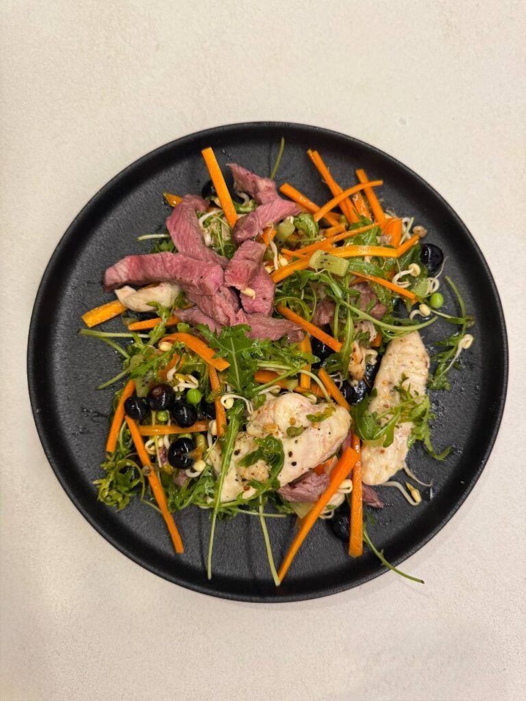Plato de ensalada con pollo, ternera, zanahoria y arándanos.