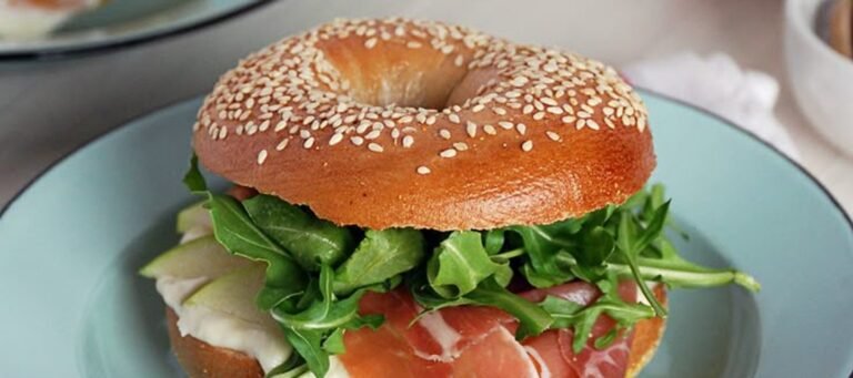 Bagel de sésamo con jamón, rúcula y manzana en un plato