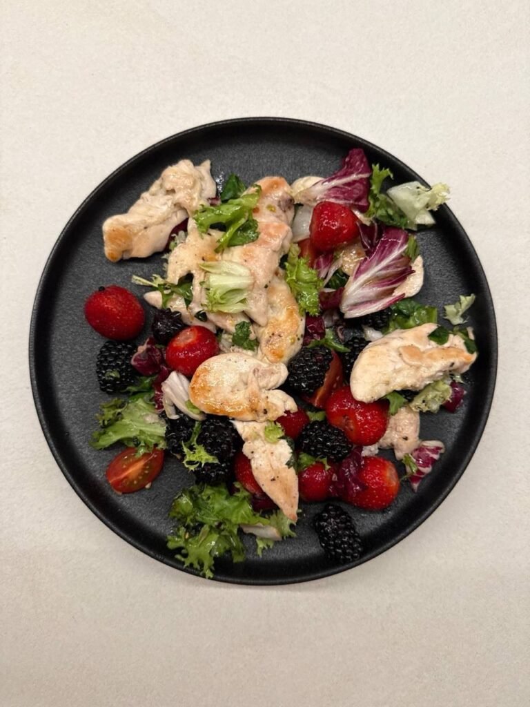 Plato de ensalada con pollo, lechuga y frutos rojos.