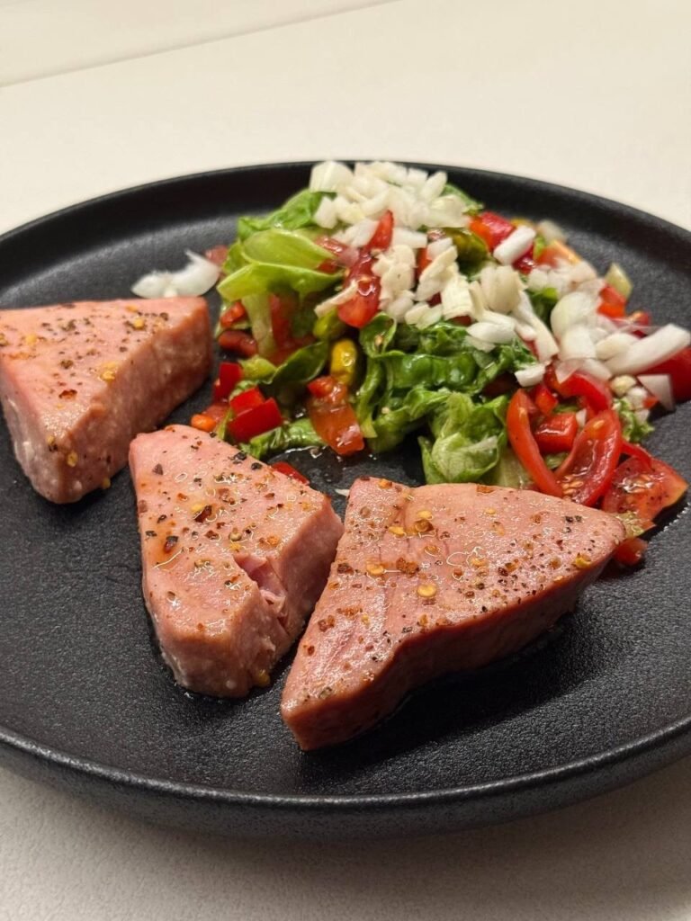 Tres piezas de atún a la plancha con ensalada de lechuga, cebolla y pimientos.