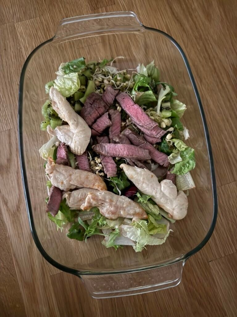 Ensalada de lechuga, pollo, ternera, brotes de soja y kiwi en una fuente de vidrio.
